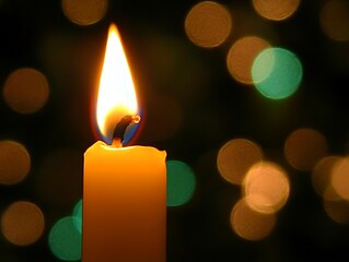 A burning candle flame glows against a blurred background of lights