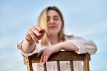 Young female artist extends paintbrush, inviting creativity. Set outdoors against serene blue sky,...