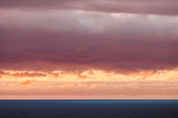 A stunning ocean view at sunset with vibrant orange and pink clouds contrasting against the calm blue water and dramatic sky