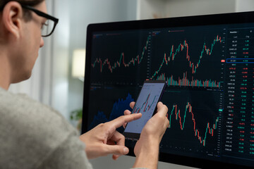 Smart stock investors pointing on screen with smartphone for market stock exchange along with laptop screen in highest dynamic investment rate, focusing data planning at modern workplace. Pecuniary.