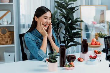 Smiling young beautiful Asian reviewing tasty mixed strawberry and cherry juice detox drinks, showing healthy product to promote for special promotion selling on social media online record. Stratagem.