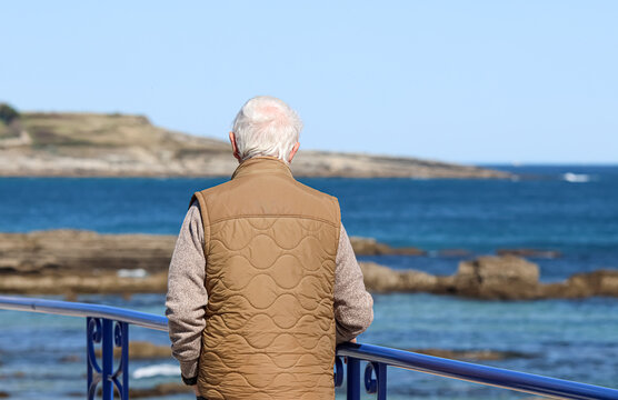 Old man with white hair walking by the sea. - Powered by Adobe