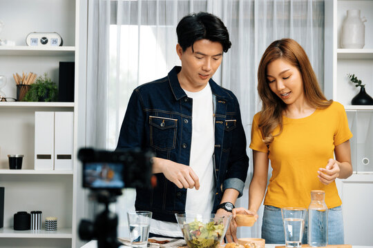 Cooking show on live streaming with two chef influencers teaching mixed salad with dressing for easy special recording on video camera. Ingredients placing bread bun wholegrain side dish. Infobahn.