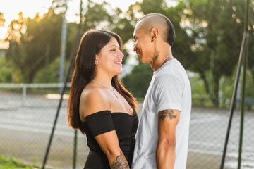 Obraz premium close-up of young latin couple, facing each other, looking into each other's eyes while smiling in love, sunset in background