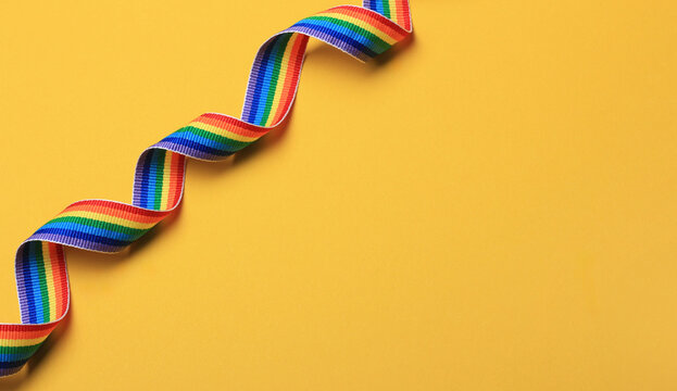 Colorful rainbow ribbon laid on a bright yellow background showcasing vibrant hues and a sense of celebration.LGBT, LGBTQ, gay pride month .