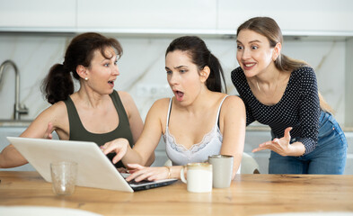 Female friends are sitting at table, reading letter on computer about invitation to study and scholarship, rejoicing at good news, are glad over victory.