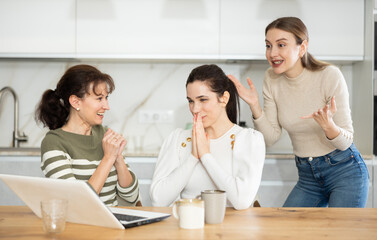 Three happy middle-aged woman expressing joy for winning standing by laptop at home