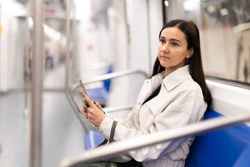 Woman sitting on seat in subway train and using smartphone