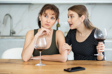 Sad and thoughtful middle-aged woman sits near kitchen table, adult relative girl ask about problems and offer help.
