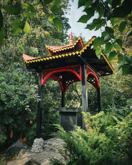 Small buddhist pavilion in a garden. Wooden gazebo surrounded by green shrubs.