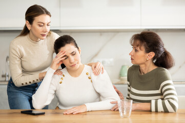 Upset woman in her middle years is seated at table supported by other kind women in the kitchen