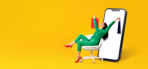 A happy customer with shopping bags relaxes in a chair while engaging with a large smartphone display. The bright background emphasizes online shopping convenience.