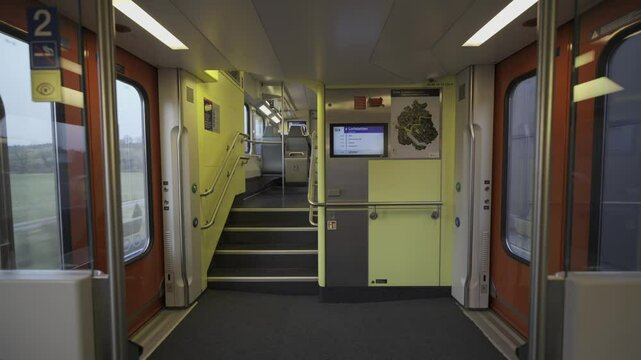 Modern double-decker Swiss train interior with stairs leading to upper level. Bright, clean design with digital display, doors and handrails. Public transport in Switzerland, commuting and travel. 