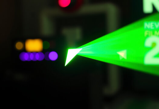 A small disc-shaped green laser emits a triangular light display against a dark background, showcasing its bright and vivid color.