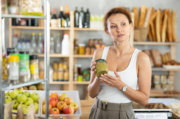 Female customer carefully choosing can of green peas in a grocery supermarket