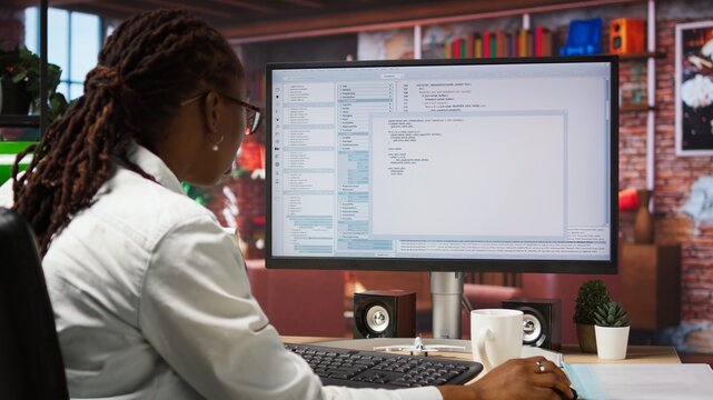 Engineer in home office looks at UI on computer monitor, typing and executing programming code. Panning shot of IT worker using coding application to write and test code in modern apartment, camera A - Powered by Adobe