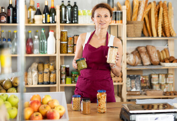 Portrait of female seller offering to buy canned green peas and beans in supermarket
