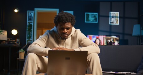 Focused man engaged in online research for a work project at home, sitting at his coffee table with...