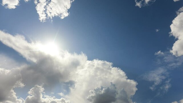 beautiful fluffy white cumulus clouds in blue sky summer season. dramatic cloud covered bright sun star in clear good atmosphere, cloudscape time-lapse of powerful sunlight beam, rays in midday,