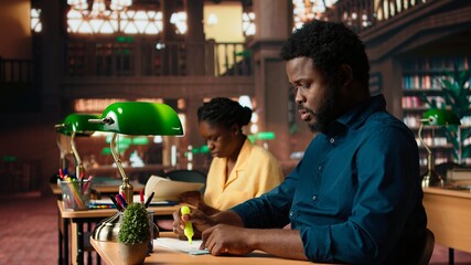 Black university student highlighting relevant phrases to learn the summary of the class lesson, memorizing key information by underlining important terms. Academic library. Camera A.