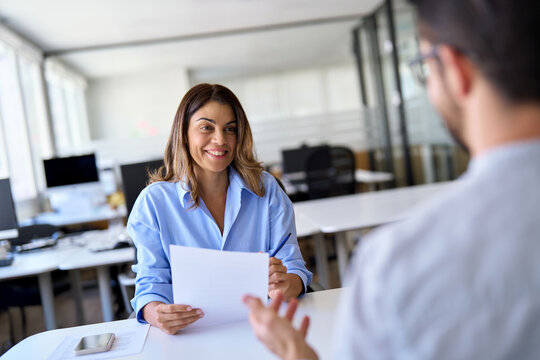 Professional female hr executive having job interview meeting with male recruit employee. Middle aged Hispanic business woman financial advisor, bank manager consulting client working in office.