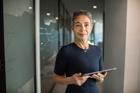 Portrait of a confident senior businesswoman holding a tablet in modern office hallway