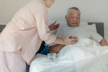 Obraz premium An elderly woman tends to her husband by administering medication while he rests in bed. The image emphasizes caregiving, compassion, and elderly support in a peaceful home setting.