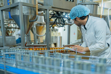 A professional factory worker inspects and monitors canned food processing on an automated assembly...