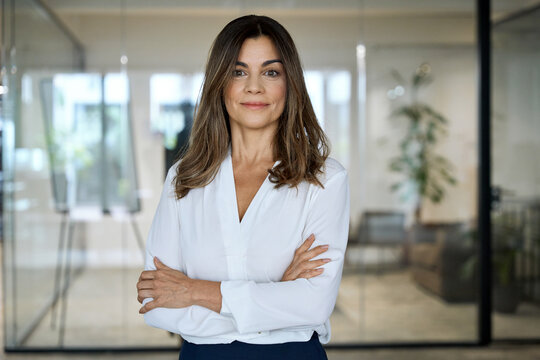 Smiling confident 45 years old professional middle aged business woman corporate leader, happy mature female executive, older lady manager standing in office arms crossed looking at camera, portrait.