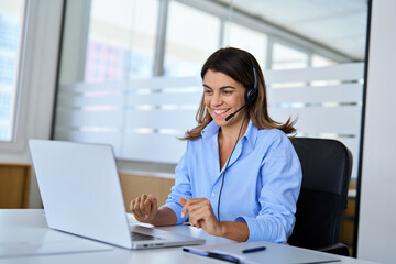 Busy happy middle aged female support service operator talking to customer sitting at desk. Smiling mature woman professional call contact center agent in headset working in office using laptop.
