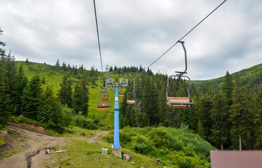 Scenic view showcasing chair lift amidst rolling green hills, dense forest, and an overcast sky....