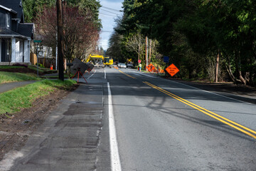 Public road works project, flagger managing traffic on one lane road, excavator in background for digging and trenching, winter construction project
