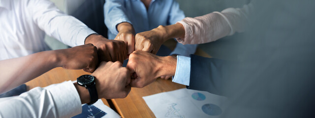Teamwork Concept. Multiethnic group of business people making fist bumps together while sitting at...