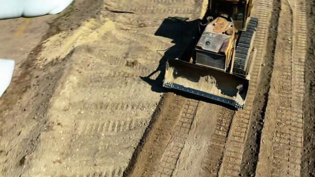 Tracking shot of yellow road grader smoothing gravel surface for highway road. Scraper leveling ground, working at construction. Earthmoving, excavations, digging on soils.