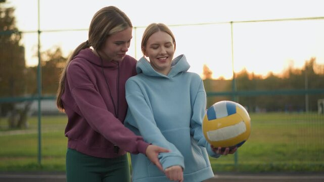 Coach teaching volleyball beginner how to serve with a warm smile on their face, both standing on outdoor court with volleyball in hand, showcasing positive energy and sportsmanship