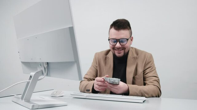 A young entrepreneur in glasses counts cash in a modern office. The concept is to show a moment of financial success, earnings, and achieving business goals.