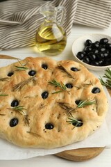 Delicious focaccia bread with olives, rosemary and oil on white table, closeup