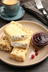 Delicious rolled crepes with cottage cheese, raisins, jam, cranberries and coffee on wooden table, closeup