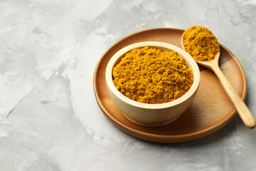 Turmeric powder in bowl and spoon on light grey table, space for text