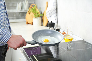 Man cooking egg in frying pan on cooktop indoors, closeup
