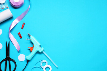 Hot glue gun and handicraft materials on light blue background, flat lay. Space for text