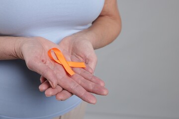 Multiple Sclerosis awareness. Woman with orange ribbon on light grey background, closeup