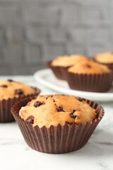 Delicious muffin with chocolate chips on white marble table, closeup