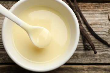 Taking tasty vanilla condensed milk with spoon from bowl on wooden table, flat lay
