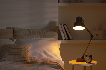 Glowing night lamp and alarm clock on bedside table indoors