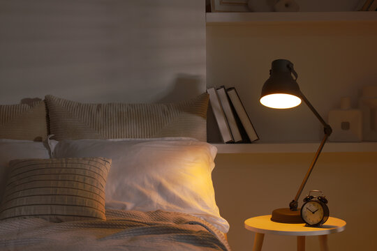 Glowing night lamp and alarm clock on bedside table indoors
