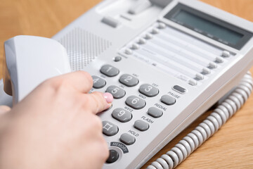 Woman dialing number on telephone at wooden table, closeup