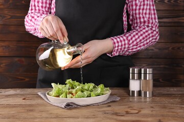 Woman pouring oil onto tasty salad at wooden table, closeup