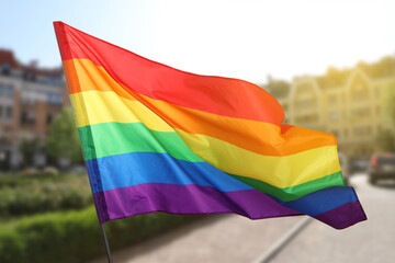 LGBT flag fluttering on city street, selective focus