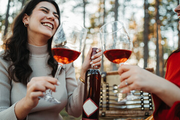 Two young caucasian woman have picnic drink wine in the forest